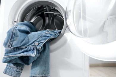 Photo of Washing machine with dirty denim jacket indoors, closeup