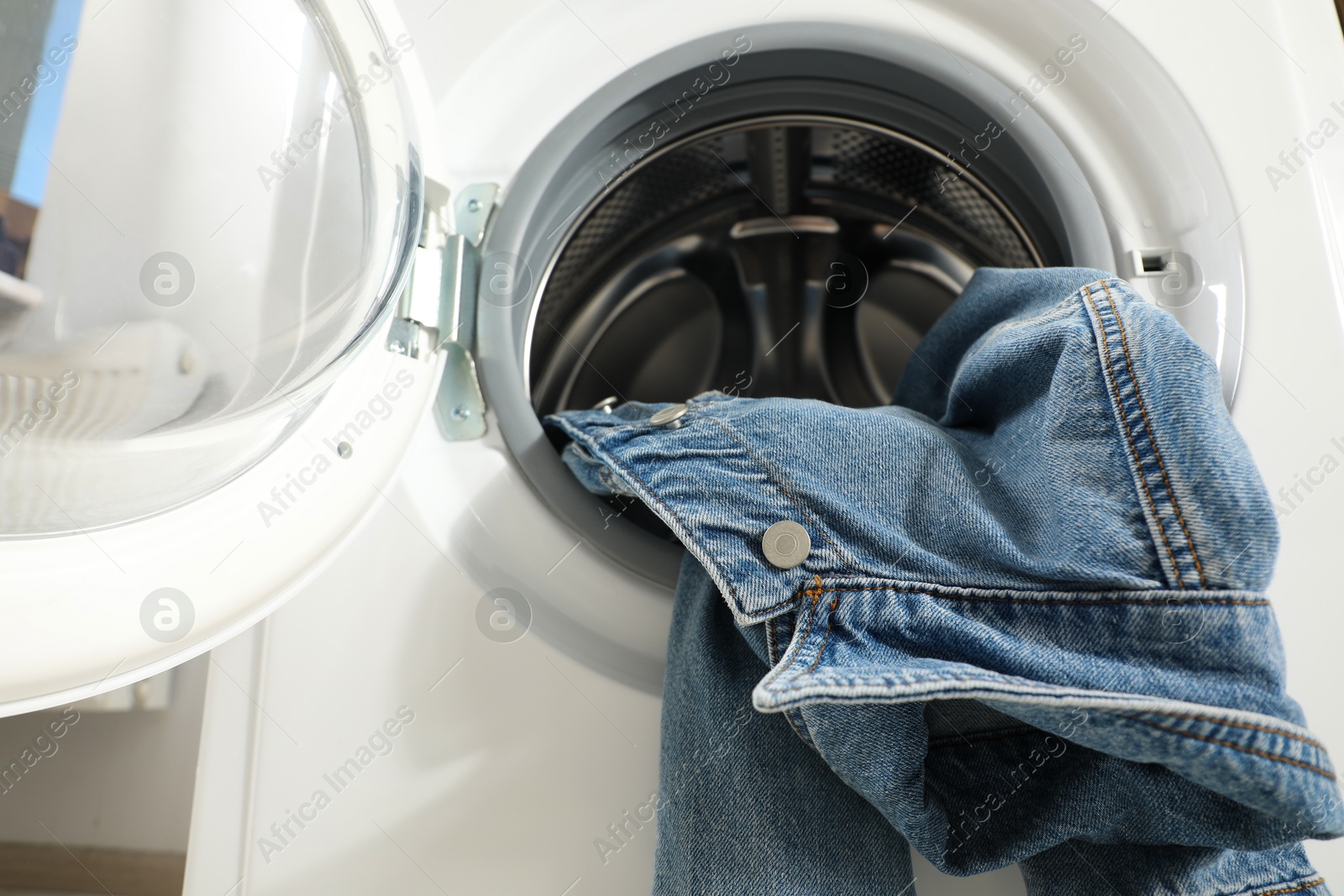 Photo of Washing machine with dirty denim jacket indoors, closeup