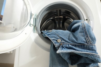 Washing machine with dirty denim jacket indoors, closeup