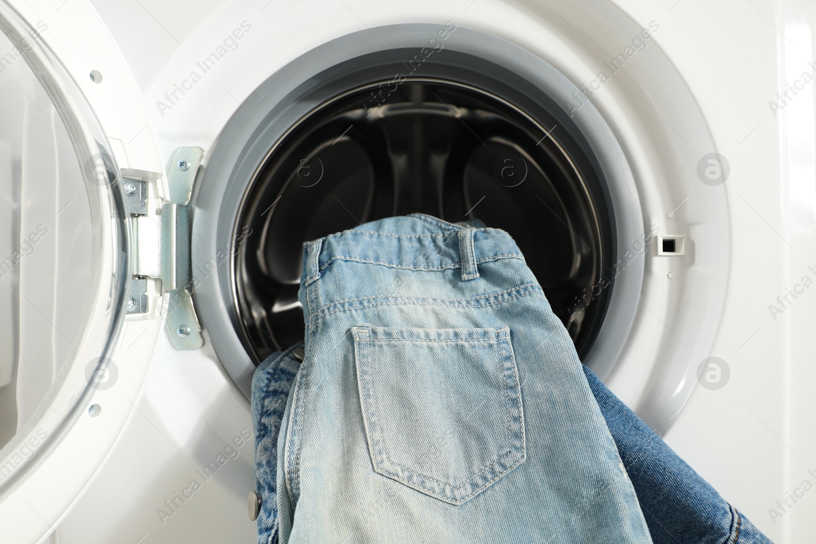 Photo of Washing machine with dirty jeans and other denim clothes indoors, closeup