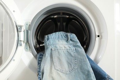 Photo of Washing machine with dirty jeans and other denim clothes indoors, closeup