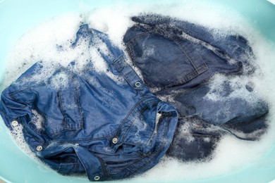 Many different denim clothes in basin with water and soap, top view