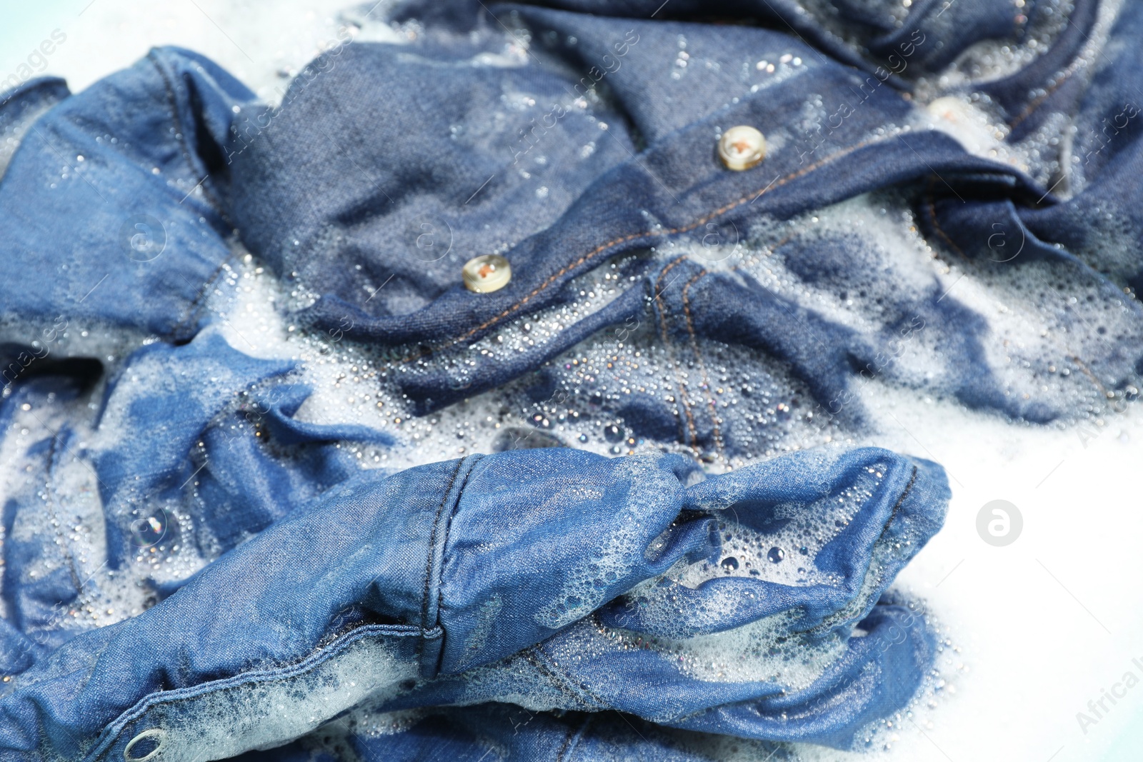 Photo of Many different denim clothes in basin with water and soap, closeup