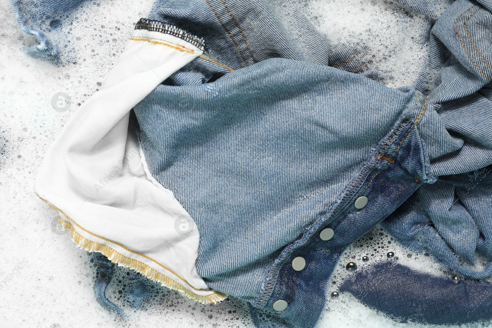 Photo of Many different denim clothes in basin with water and soap, top view