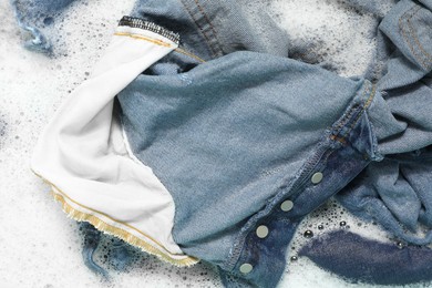 Many different denim clothes in basin with water and soap, top view