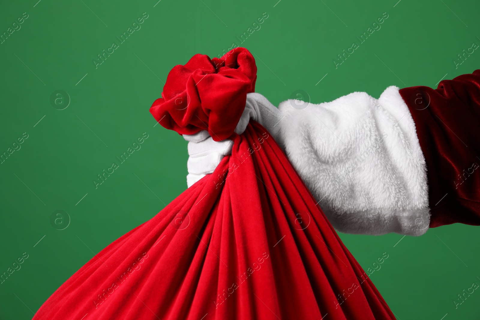 Photo of Santa Claus with red bag of Christmas gifts on green background, closeup