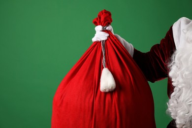 Photo of Santa Claus with red bag of Christmas gifts on green background, closeup