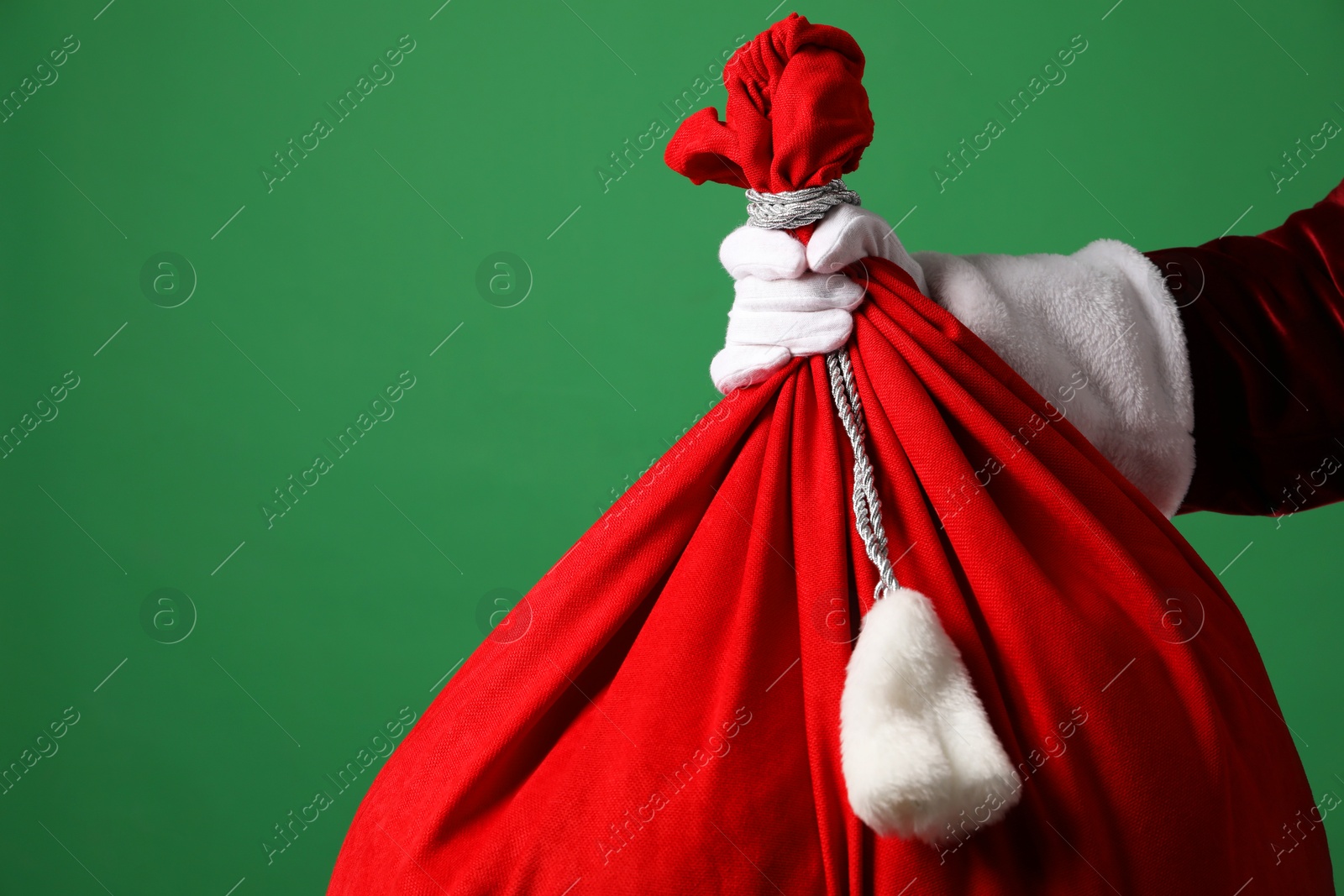 Photo of Santa Claus with red bag of Christmas gifts on green background, closeup