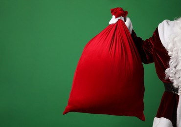 Photo of Santa Claus with red bag of Christmas gifts on green background, closeup. Space for text