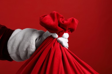 Photo of Santa Claus with bag of Christmas gifts on red background, closeup