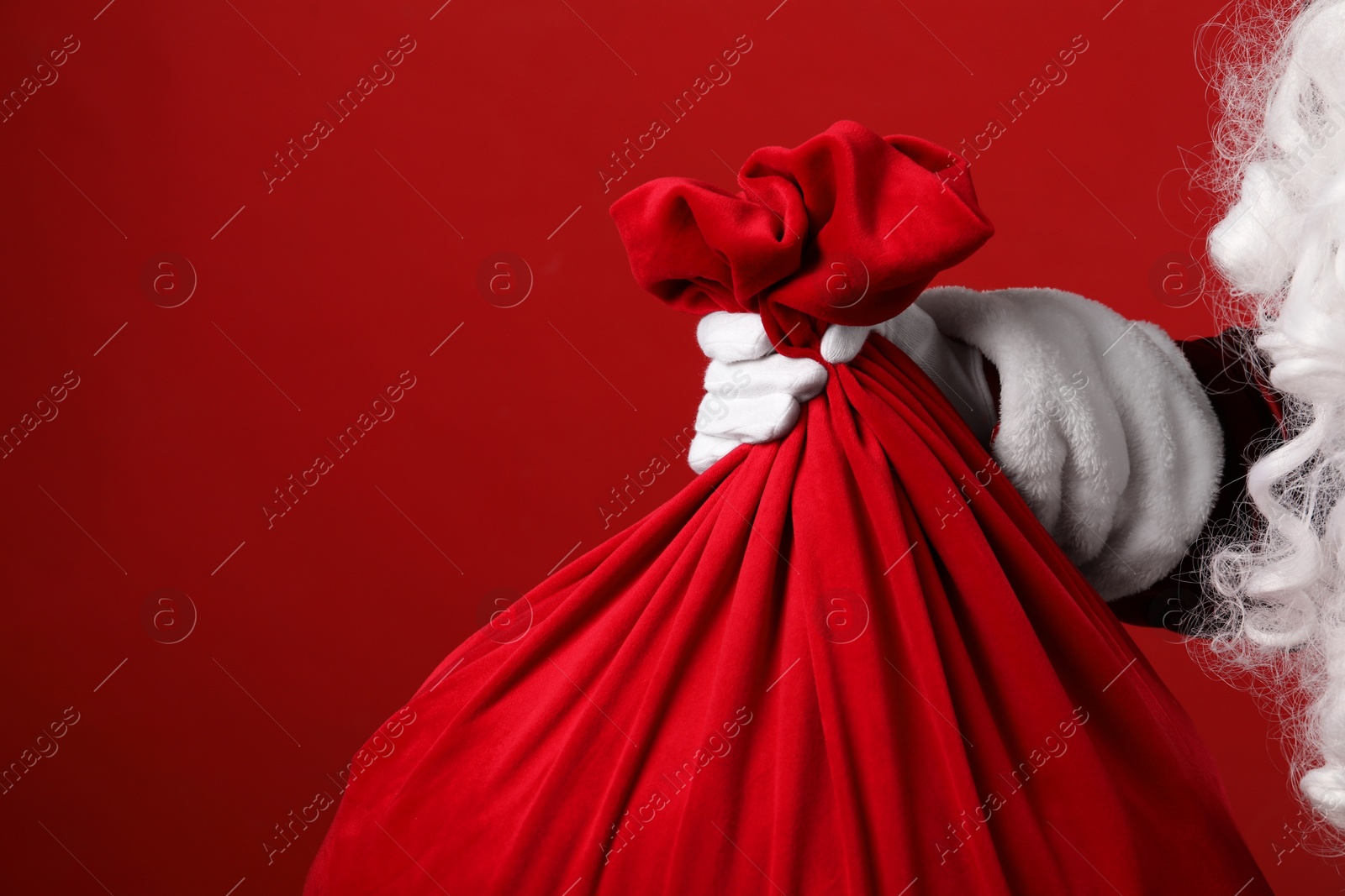 Photo of Santa Claus with bag of Christmas gifts on red background, closeup