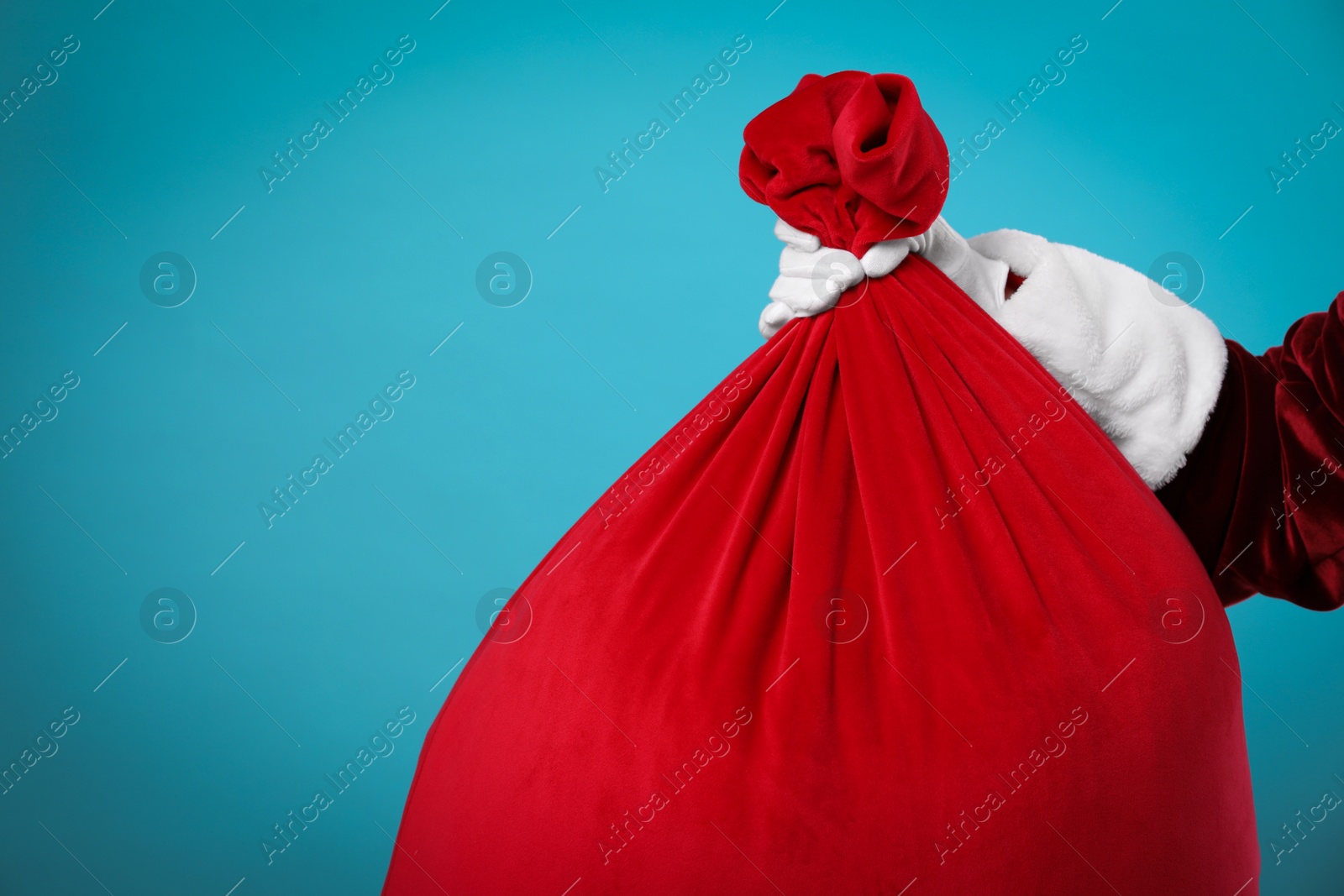 Photo of Santa Claus with red bag of Christmas gifts on light blue background, closeup