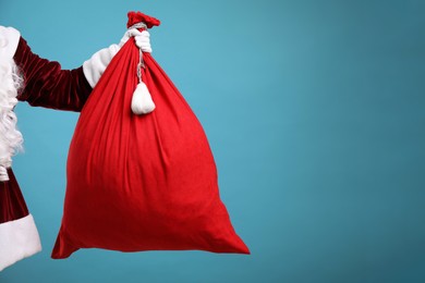 Photo of Santa Claus with red bag of Christmas gifts on light blue background, closeup. Space for text