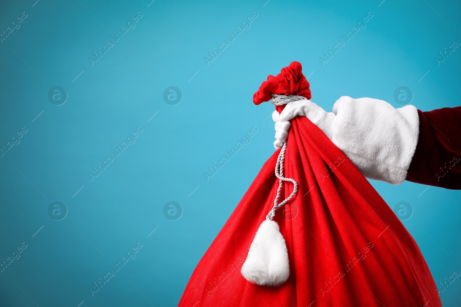 Photo of Santa Claus with red bag of Christmas gifts on light blue background, closeup. Space for text