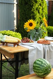 Photo of Ripe watermelon on wooden bench near table with fresh products and sunflowers in garden