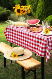 Photo of Fresh fruits, pie and vase with sunflowers on table in garden