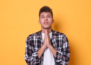 Photo of Young student praying for good exam result on yellow background