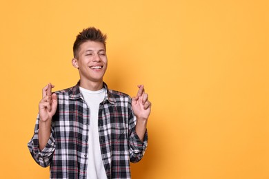 Photo of Excited young student crossing fingers on yellow background, space for text. Hope for good exam result