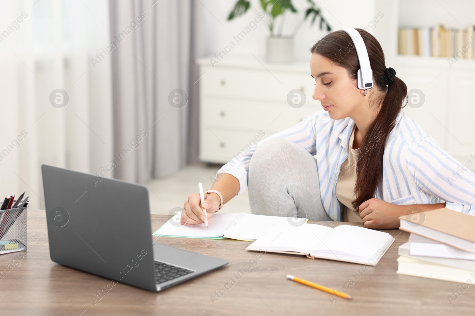 Photo of Student in headphones studying at wooden table indoors