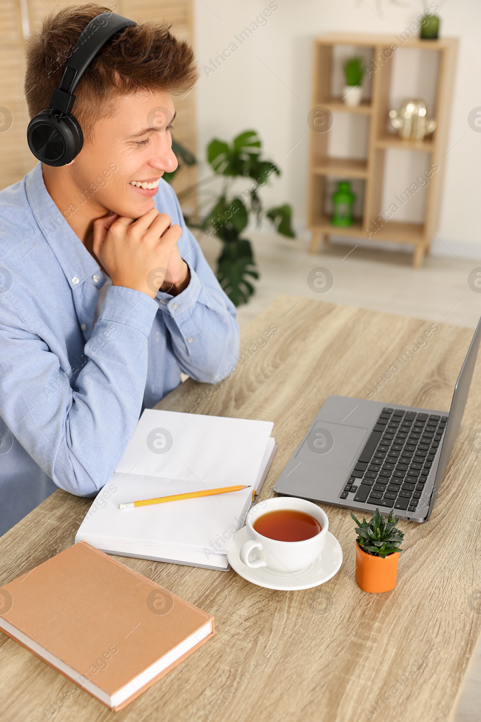 Photo of Student in headphones studying at wooden table indoors