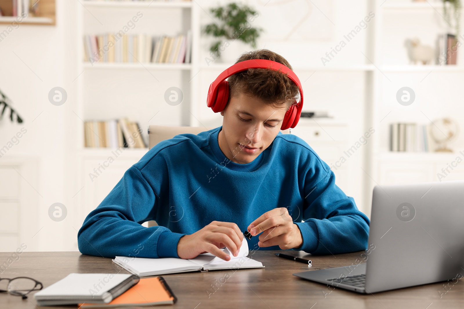 Photo of Student in headphones studying at wooden table indoors