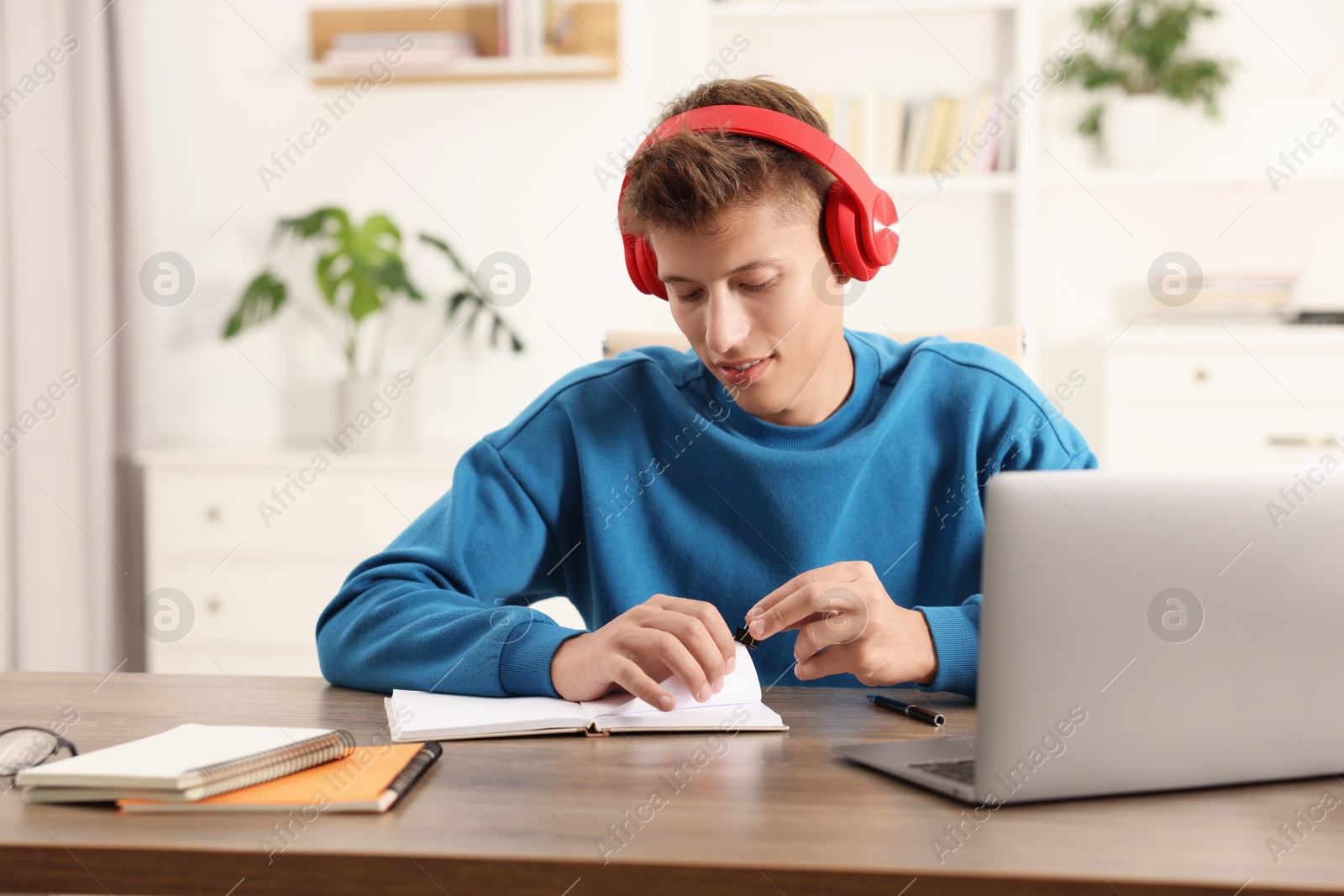 Photo of Student in headphones studying at wooden table indoors