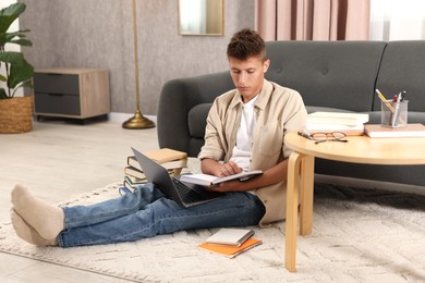 Photo of Student with book and laptop studying on floor at home