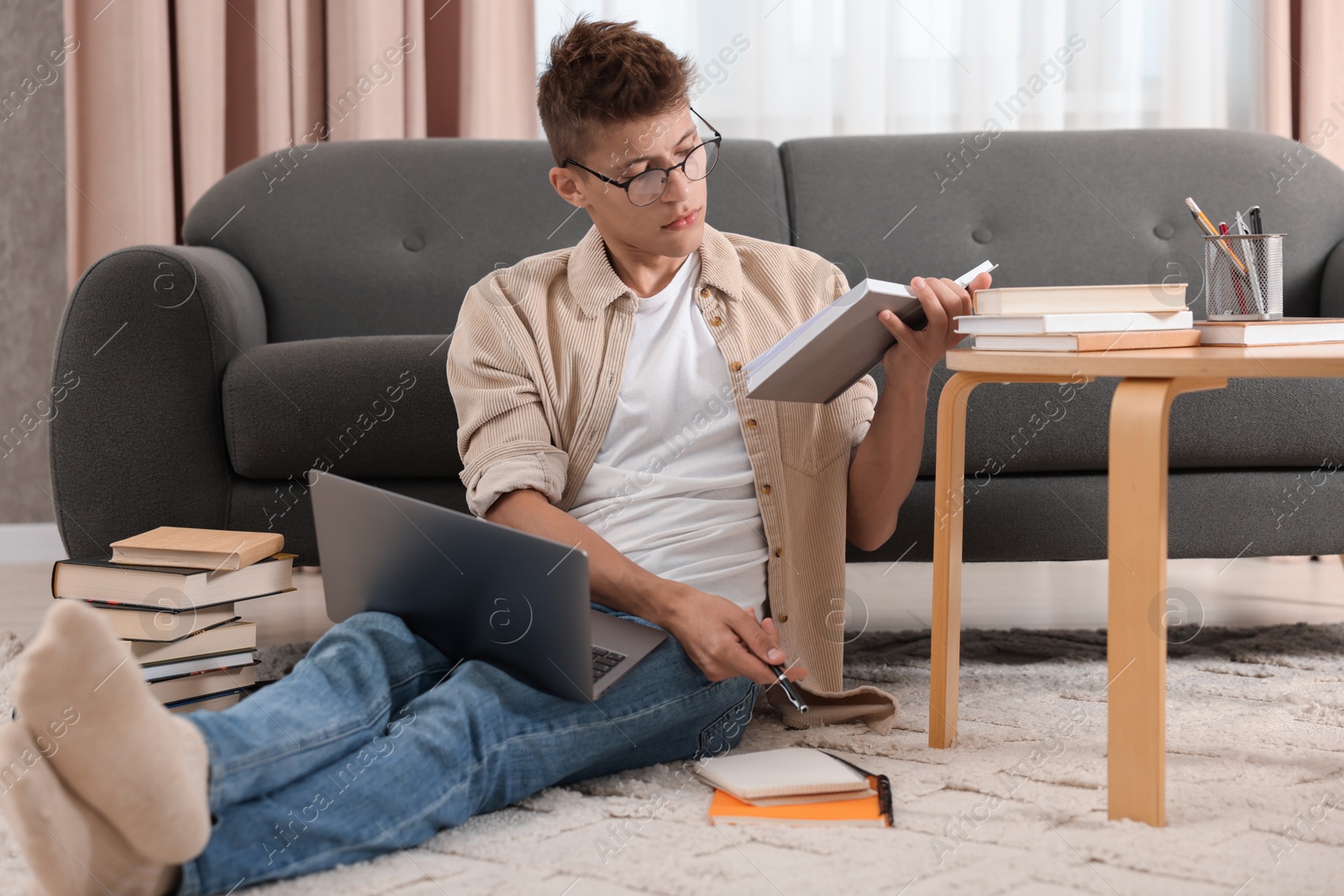 Photo of Student with book and laptop studying on floor at home