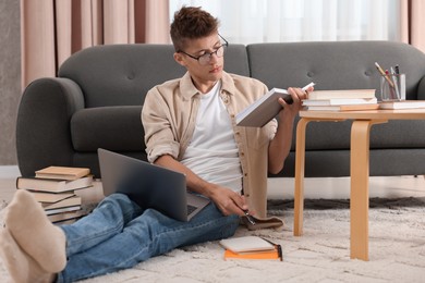 Student with book and laptop studying on floor at home