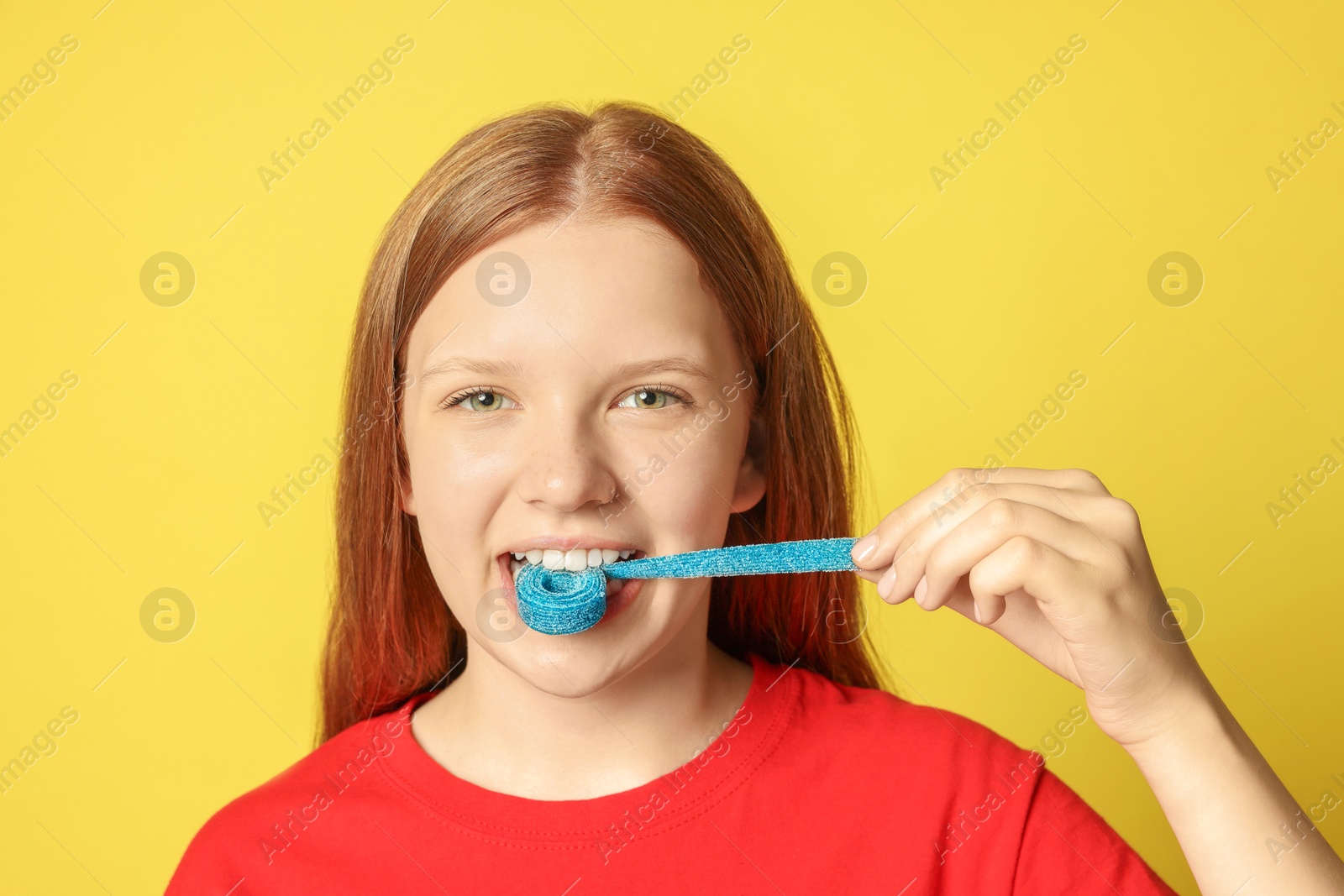 Photo of Teenage girl eating tasty gummy candy on yellow background