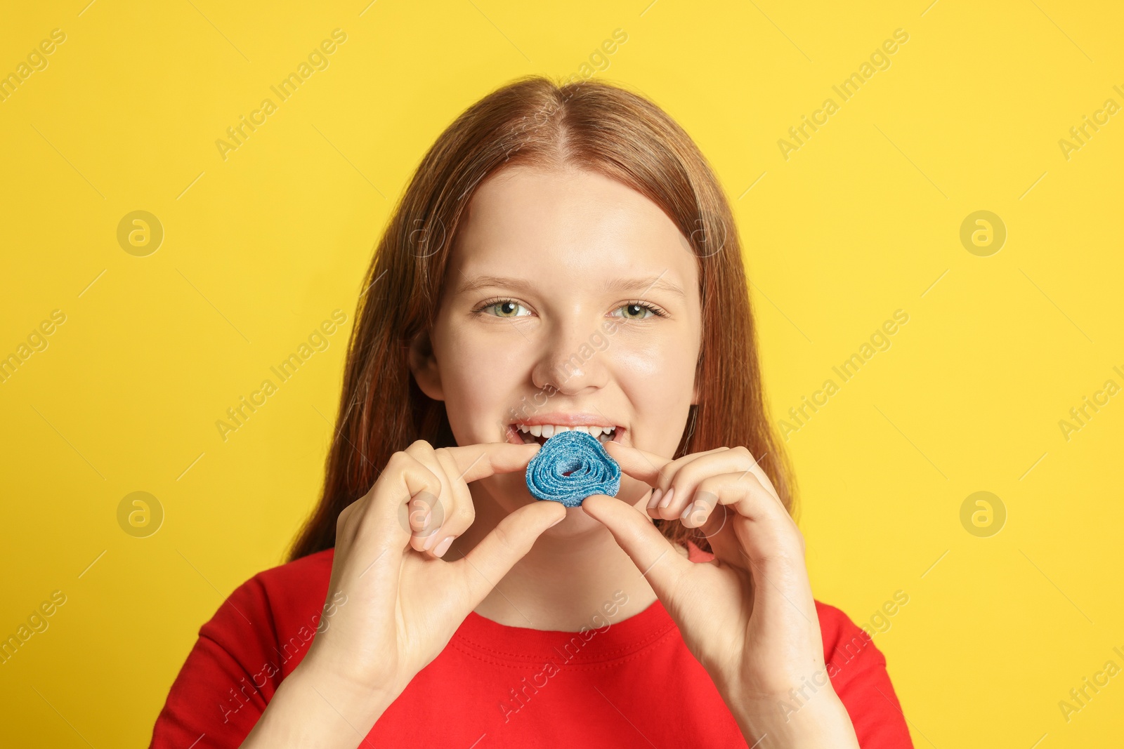 Photo of Teenage girl eating tasty gummy candy on yellow background