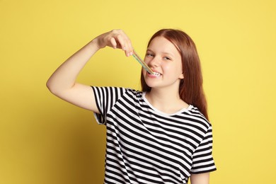 Teenage girl eating tasty rainbow sour belt on yellow background