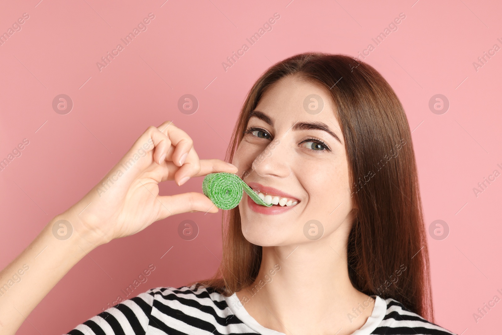 Photo of Young woman eating tasty gummy candy on pink background