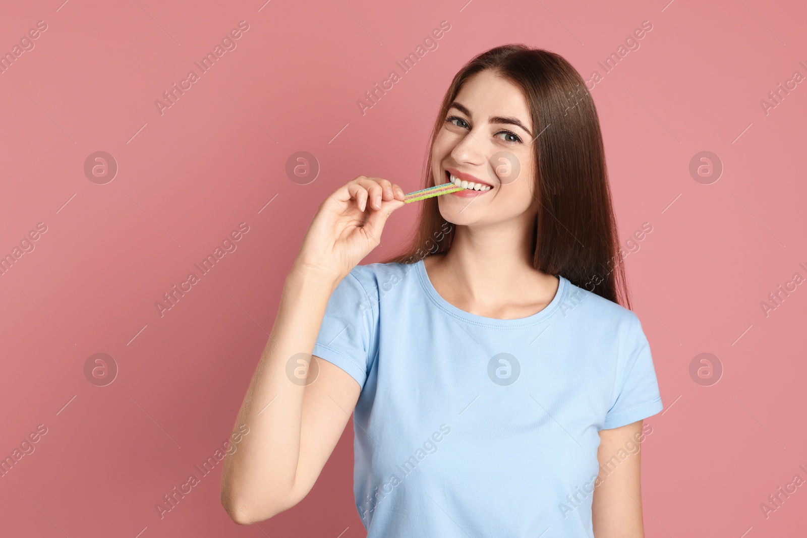 Photo of Young woman eating tasty rainbow sour belt on pink background