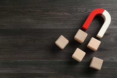 Photo of Magnet attracting cubes on wooden table, flat lay. Space for text