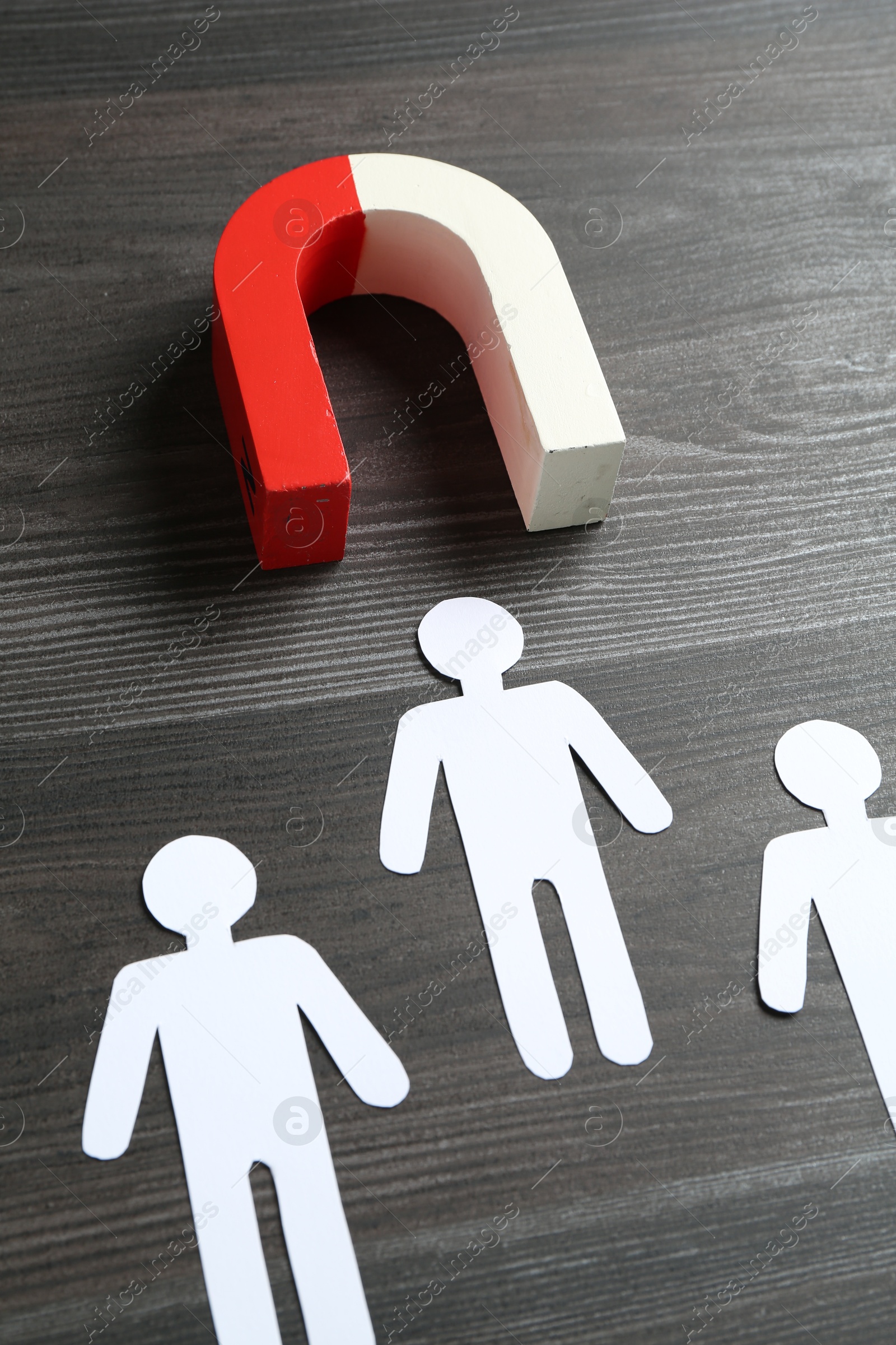 Photo of Magnet attracting paper human figures on wooden table, closeup