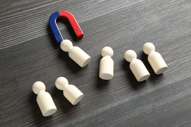 Photo of Magnet attracting human figures on wooden table, closeup