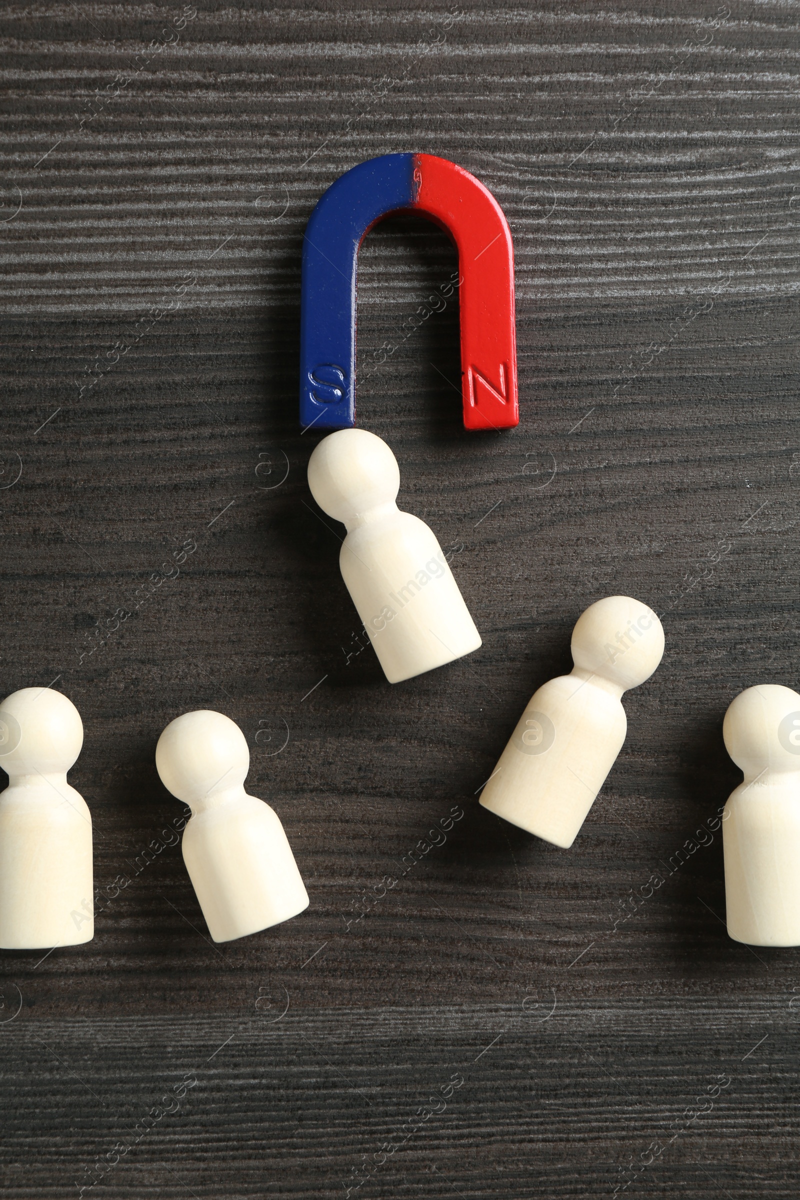 Photo of Magnet attracting human figures on wooden table, flat lay