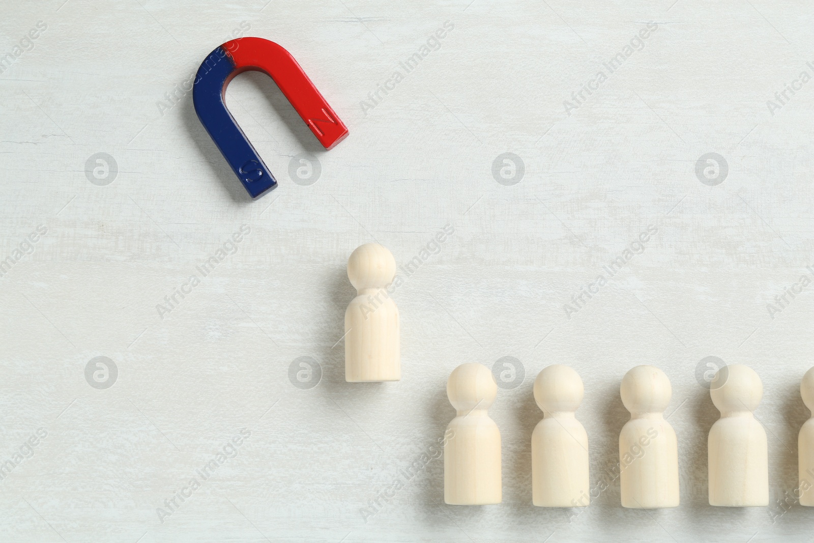 Photo of Magnet attracting human figure among other ones on white table, flat lay