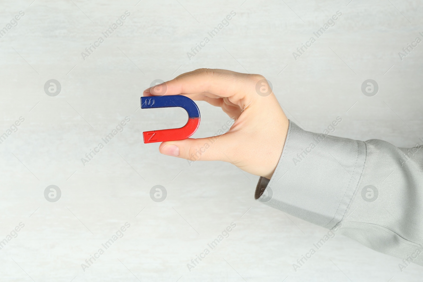 Photo of Woman with horseshoe magnet on light background, closeup