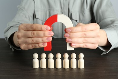 Photo of Woman with magnet attracting human figures at wooden table, closeup