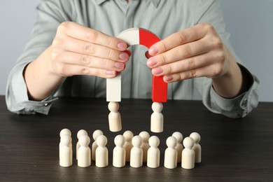 Photo of Woman with magnet attracting human figures at wooden table, closeup