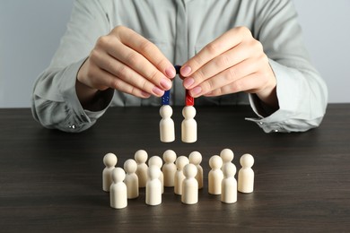 Photo of Woman with magnet attracting human figures at wooden table, closeup