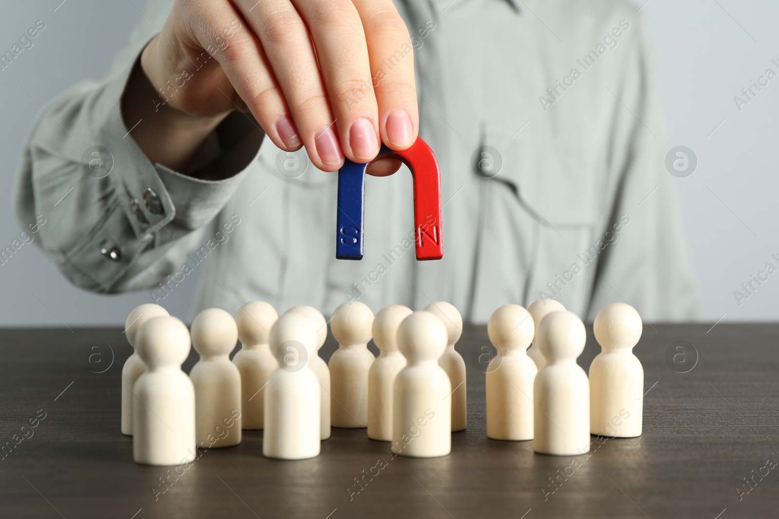 Photo of Woman with magnet attracting human figures at wooden table, closeup