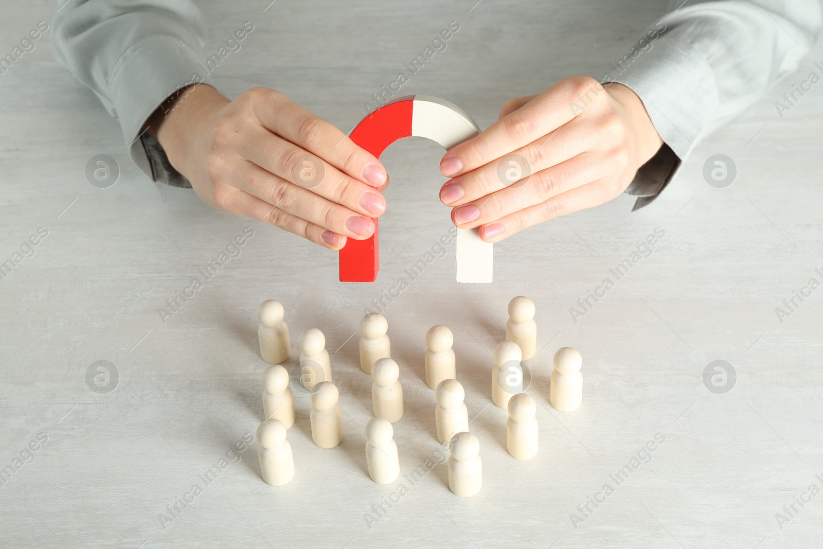 Photo of Woman with magnet attracting wooden human figures at light table, closeup