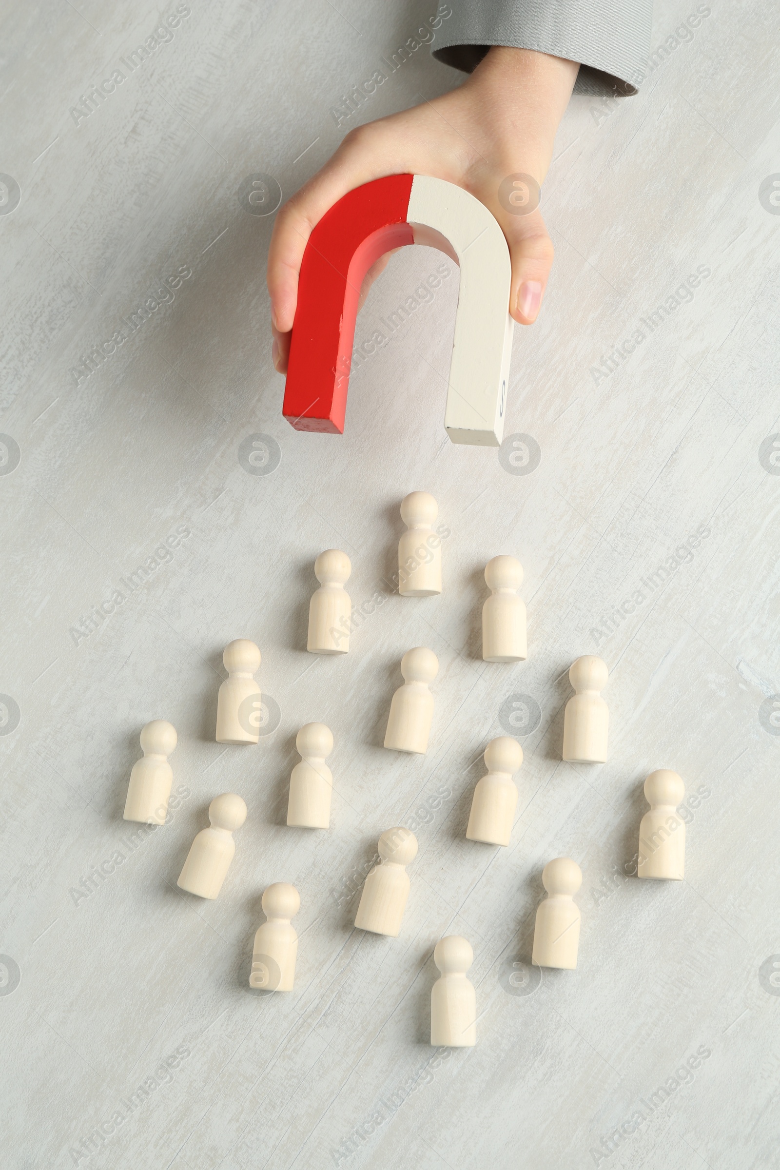 Photo of Woman with magnet attracting wooden human figures at light table, top view