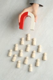 Photo of Woman with magnet attracting wooden human figures at light table, top view