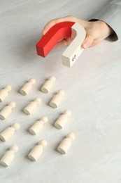 Photo of Woman with magnet attracting wooden human figures at light table, above view