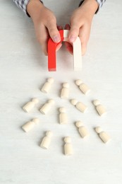 Photo of Man with magnet attracting wooden human figures at light table, above view