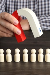 Photo of Man with magnet attracting human figures at wooden table, closeup